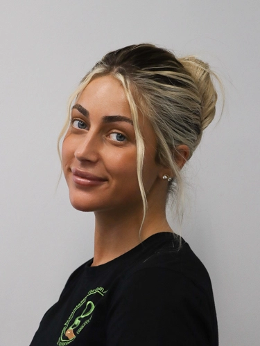 Professional headshot of a woman with blonde hair in a loose bun, smiling against a plain light background.